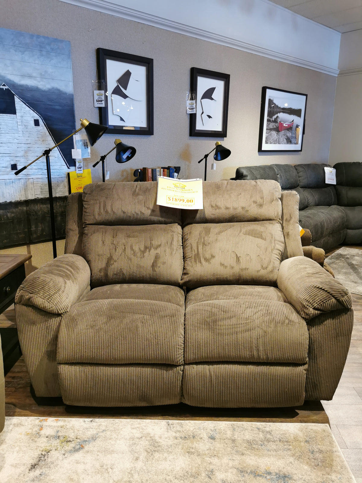 The La-Z-Boy 761 Joel Power Reclining Loveseat in textured brown fabric sits elegantly in the showroom. Framed art complements its design, and a price tag of $1,799.00 adorns the backrest. Cushioned arm pads enhance its comfort and inviting appeal.