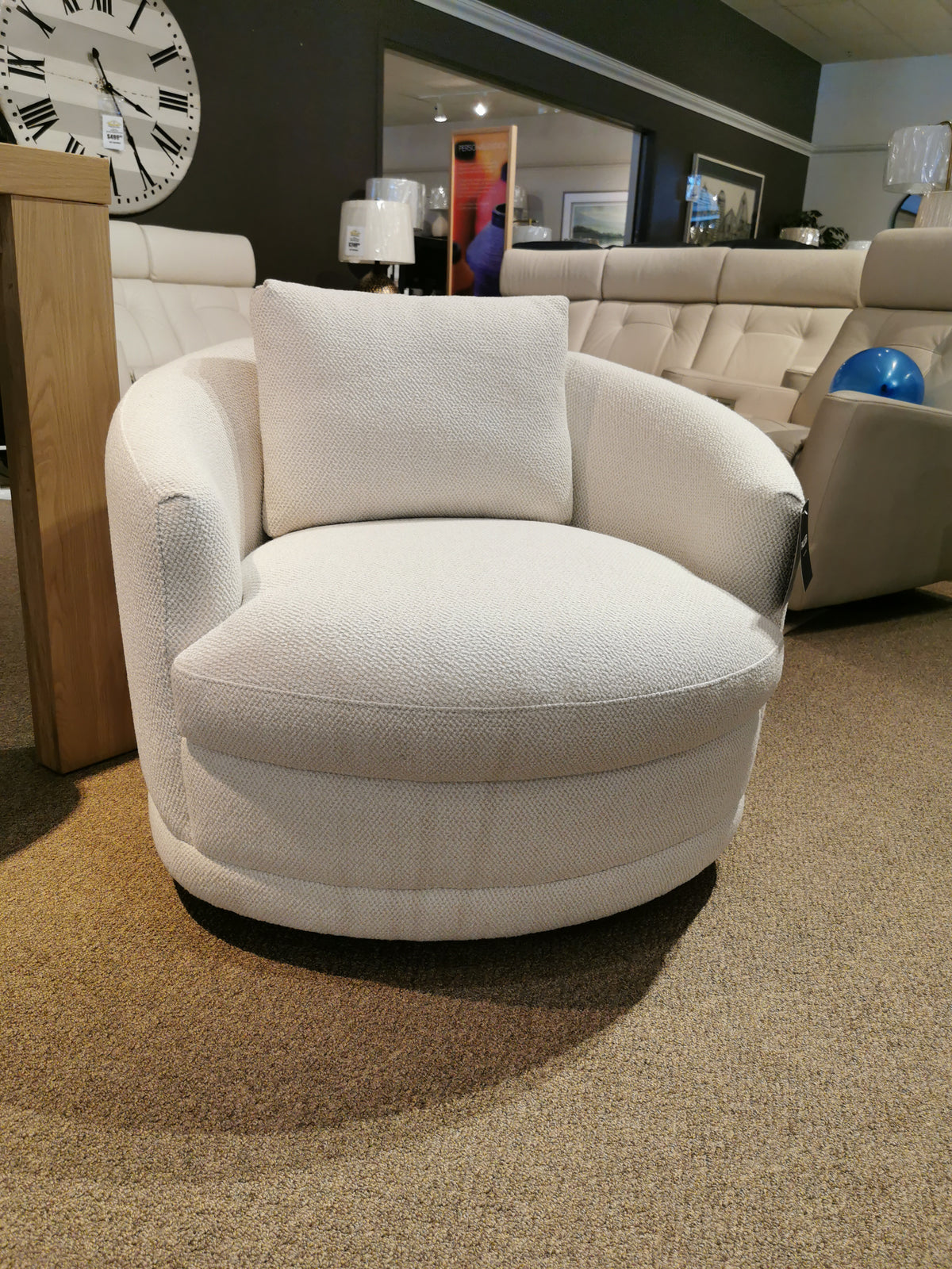 A white, round Kinsley Swivel Chair by Palliser is elegantly displayed in the furniture showroom, its cushioned comfort complemented by a stylish label on the side.