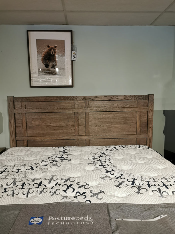 A made 123 Architectural King Bed by Vaughan Bassett with a wooden headboard and patterned bedding has a bear photo above.