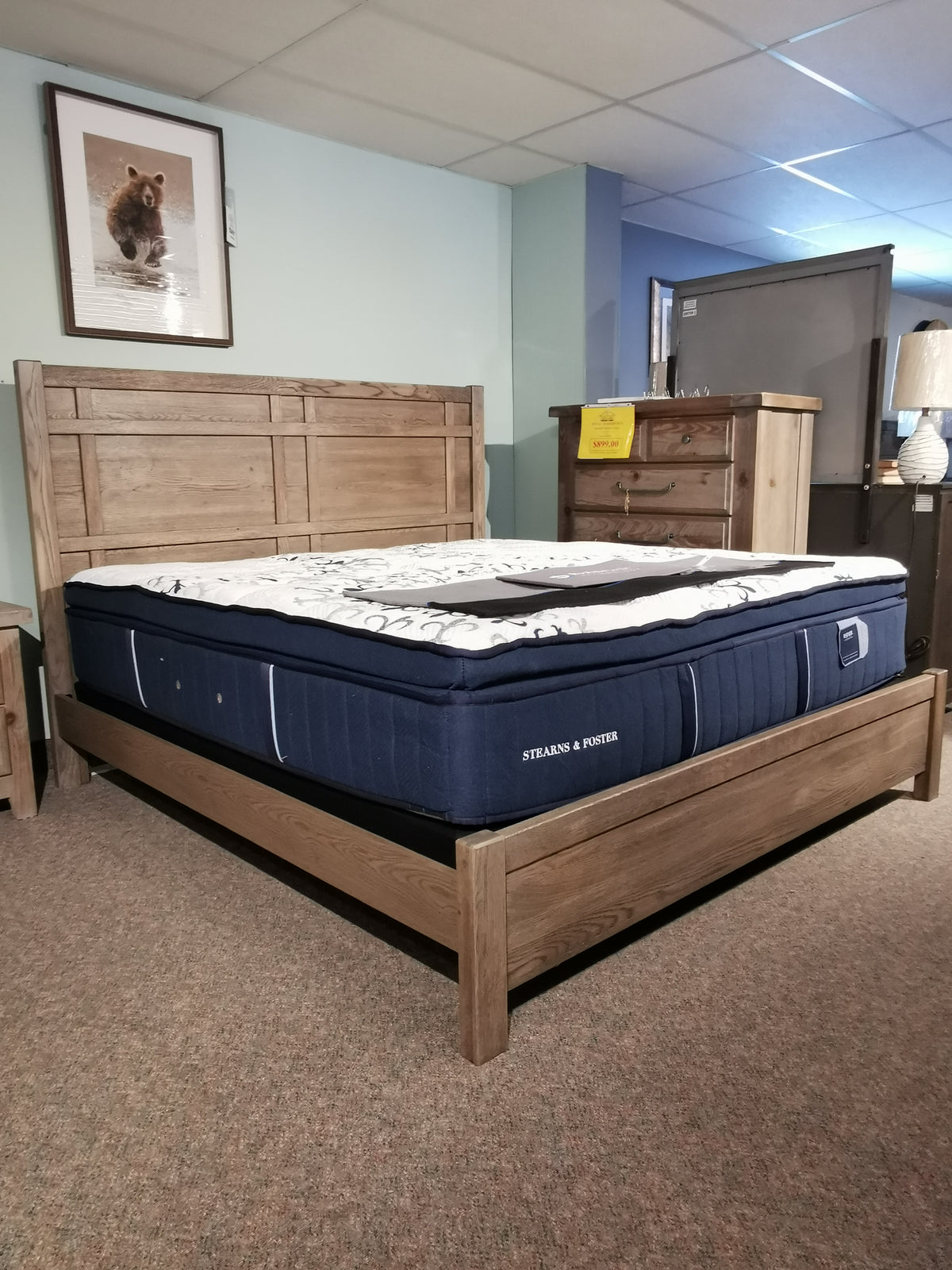 A Vaughan Bassett 123 Architectural King Bed in Solid American White Oak with a blue mattress, next to a dresser and lamp.