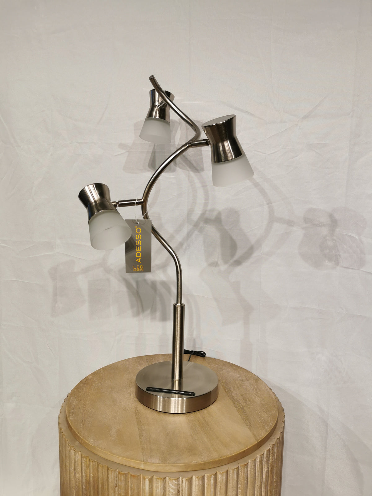 Adesso Cyrus Table Lamp with LED touch switch, three adjustable heads, set on a wooden table against a plain backdrop.