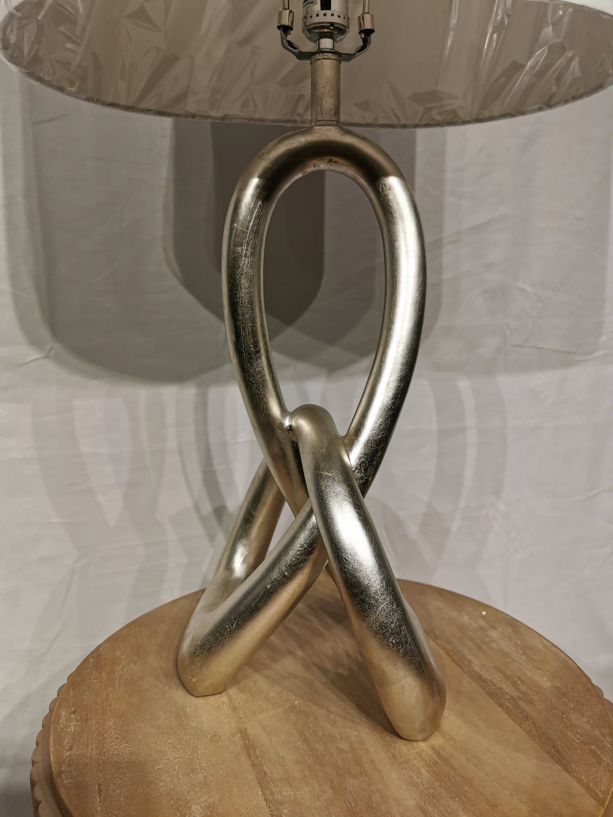 A ST. James Sculptural Knot Table Lamp by Crestview Collection graces a table with its gilded silver base and white shade.