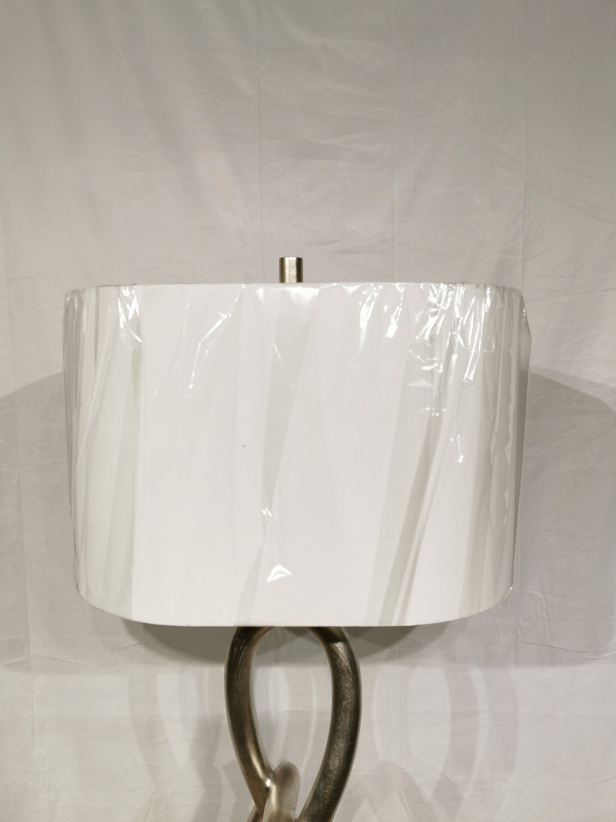 A white shade wrapped in plastic on Crestview's St. James Sculptural Knot Lamp with gilded silver finish.