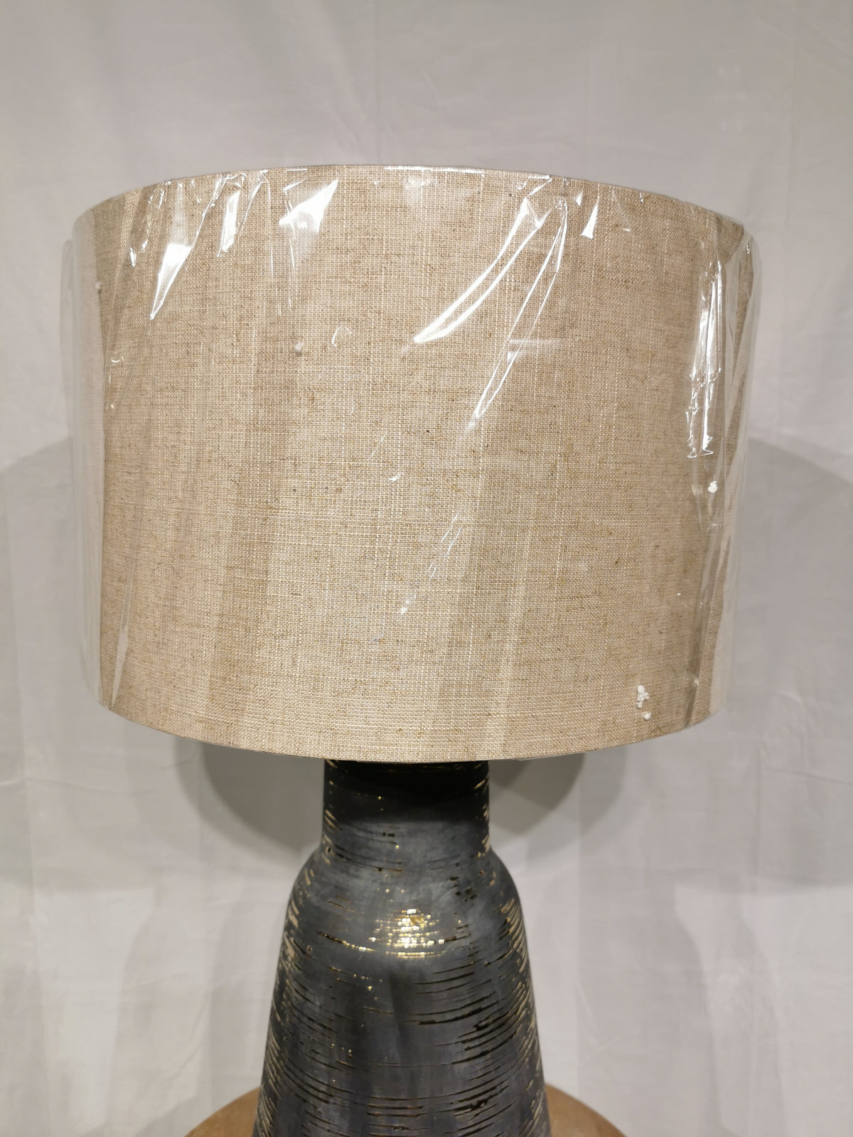 The Crestview Collection Trinity Table Lamp features a wrapped beige shade and textured charcoal ceramic base on a white backdrop.