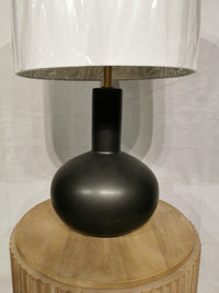 The Crestview Collection Griffith Table Lamp has a matte ceramic base, white shade, and sits on a round wooden surface.