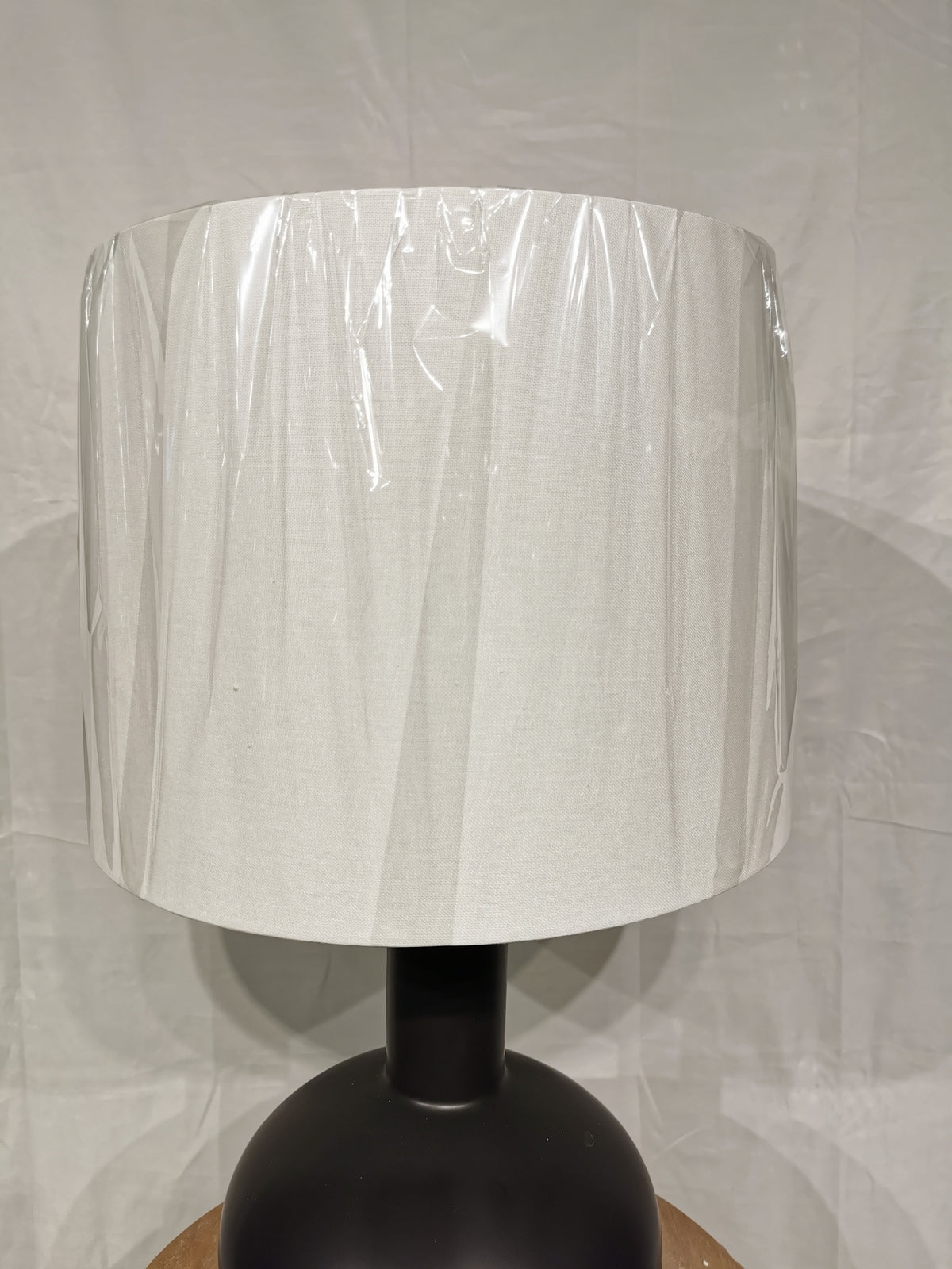 The Crestview Collection Griffith Table Lamp, with a white shade in plastic, rests on a wood surface against a white backdrop.