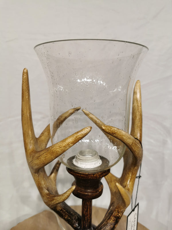 The Crestview Collection's Huxley Antler Table Lamp has a glass holder and rustic deer antler-style base on wood.