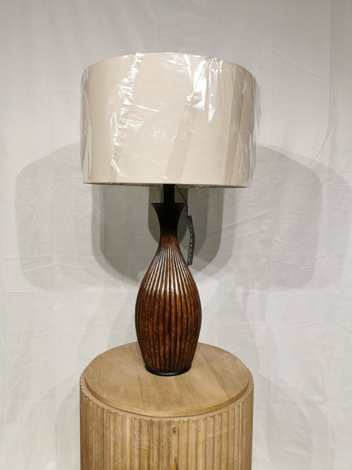 The Crestview Collection Bronze Resin Table Lamp illuminates, featuring a wooden fluted base and wrapped beige shade.