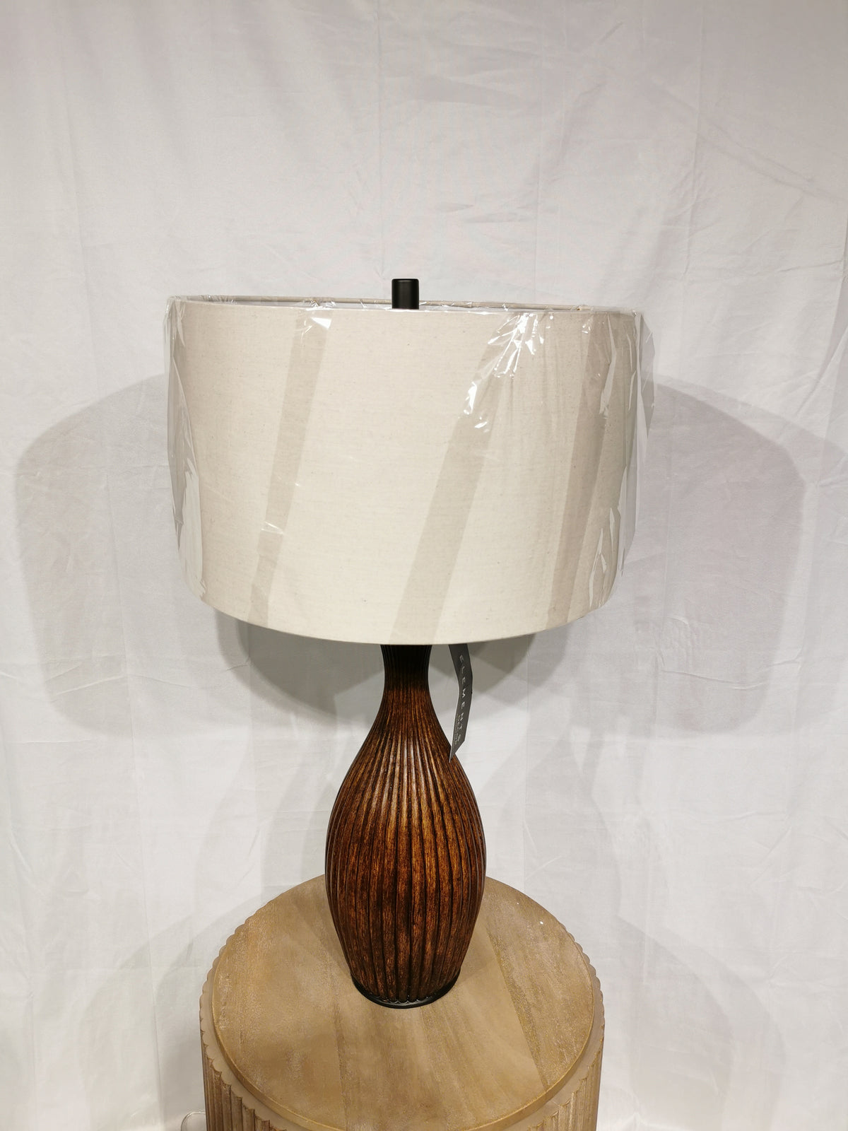 The Crestview Collection Bronze Resin Table Lamp features a ribbed base, large beige shade, and sits on a round table.