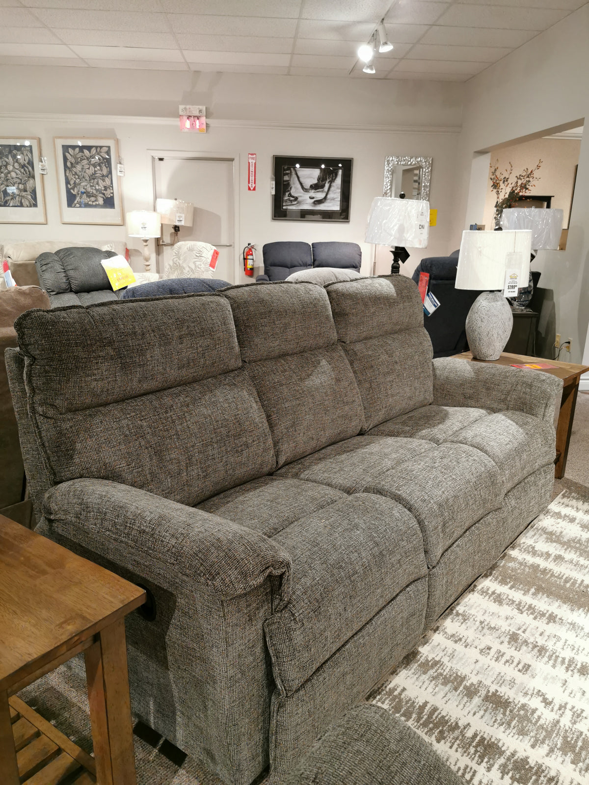 706 Jay Sofa by La-z-boy, a gray upholstered recliner, displayed with lamps and tables in a furniture store.