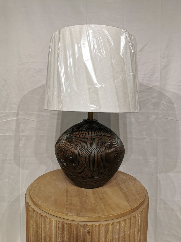 The Crestview Collection's Reine Table Lamp has a white shade, black base with Aztec hints, and a round wooden pedestal.