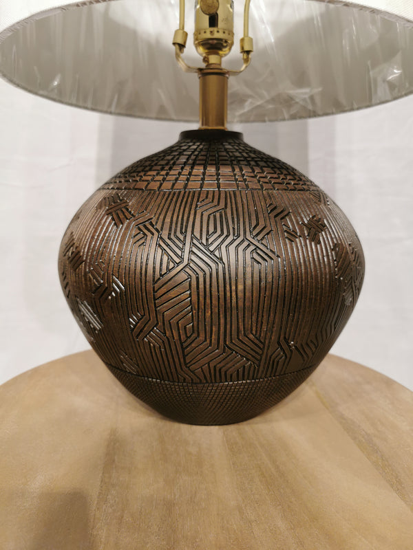 Close-up of Crestview Collection's Reine Table Lamp, featuring an Aztec design on its bronze base and a white shade.