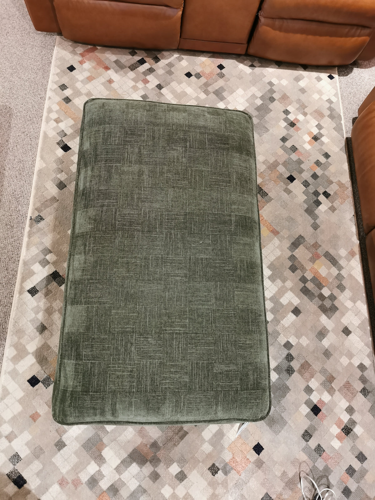 A green Cory 205 Storage Ottoman by La-Z-Boy sits on a patterned rug, surrounded by parts of a brown couch.