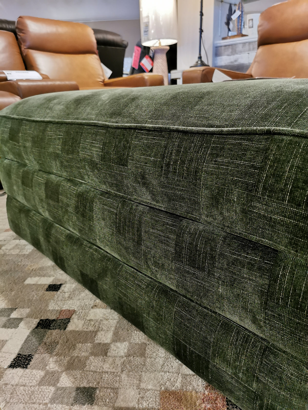 Cory 205 storage ottoman by La-Z-Boy on patterned rug with brown leather chairs and a lit lamp in the background.