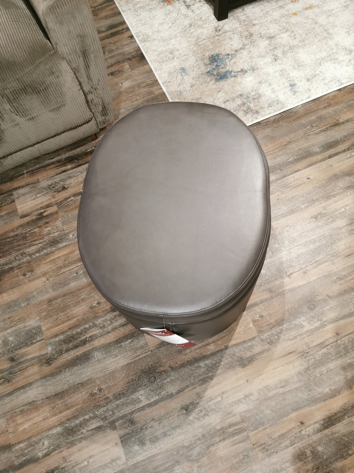 A gray Maeve 402 Storage Ottoman by La-z-boy on a wooden floor with hidden casters near a sofa.