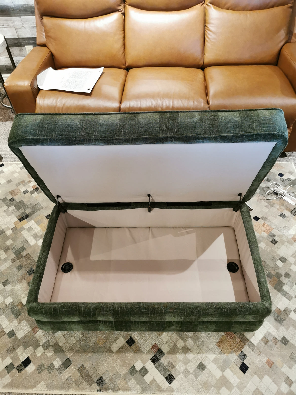 La-z-boy's Cory 205 Storage Ottoman features a green fabric exterior for easy mobility in front of a brown leather couch.