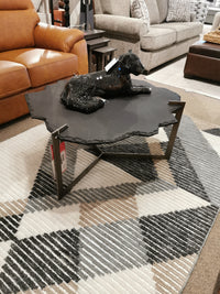 A modern living room display with Mercana's 69049 Shale Coffee Table, a decorative dog sculpture, and patterned rug.