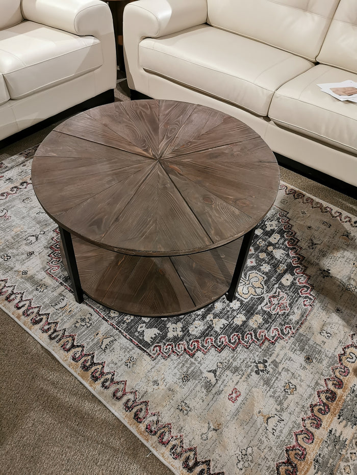 The Crestview Collection Jackson Round Coffee Table enriches the living space on a patterned rug, surrounded by white sofas.