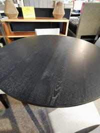 The Rory 48" Dining Package by Donald Choi features a round black oak table and light gray chairs in a showroom setup.