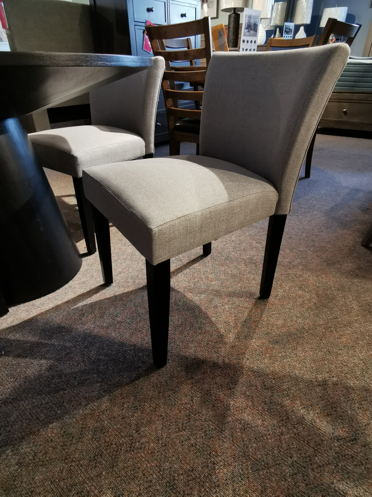 Two upholstered chairs with dark wooden legs stand by a compact table in the Donald Choi Rory 48" Dining Package.