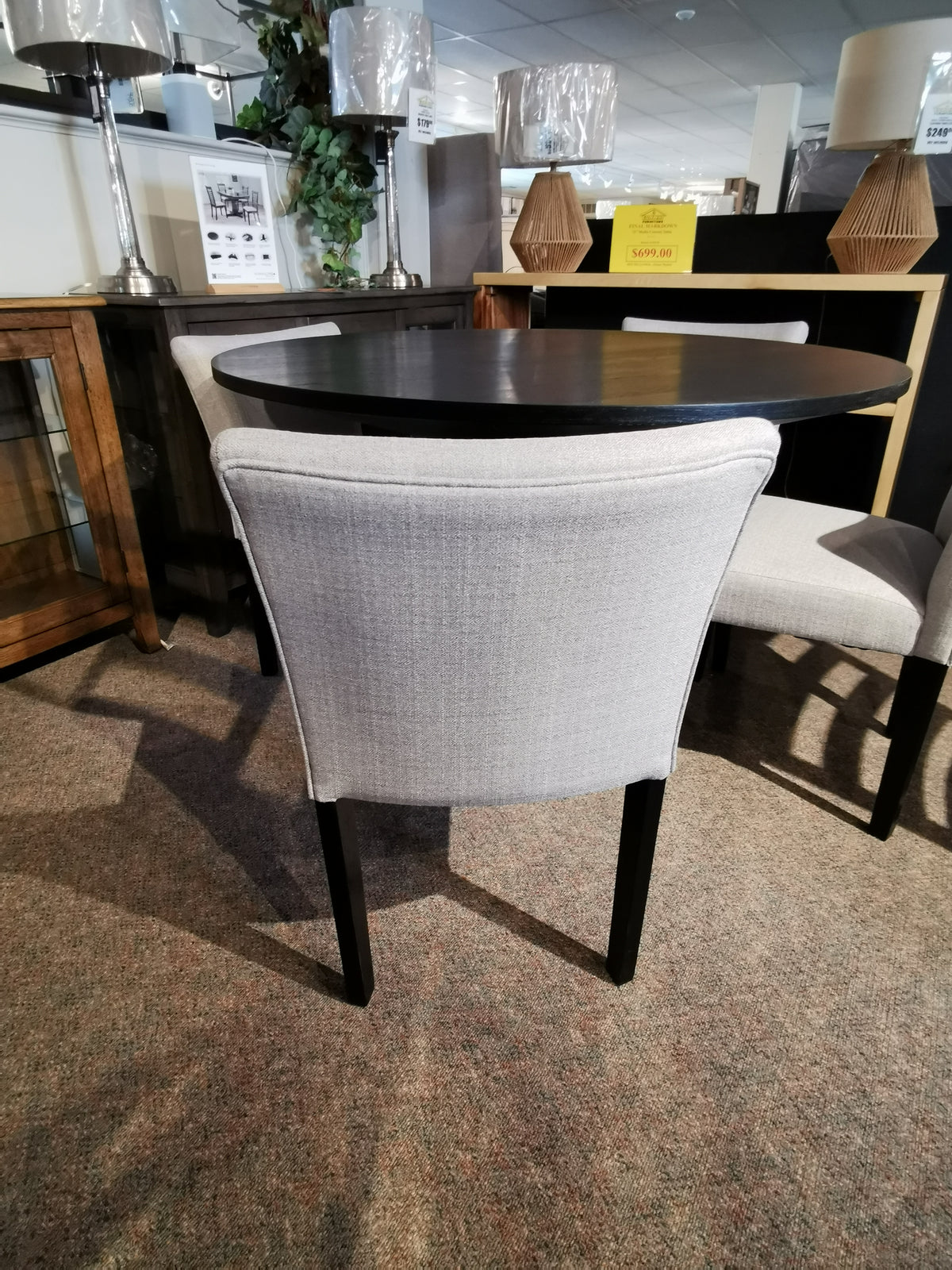 Gray upholstered chairs encircle the Rory 48" Dining Package's compact black oak veneer table in a carpeted showroom.