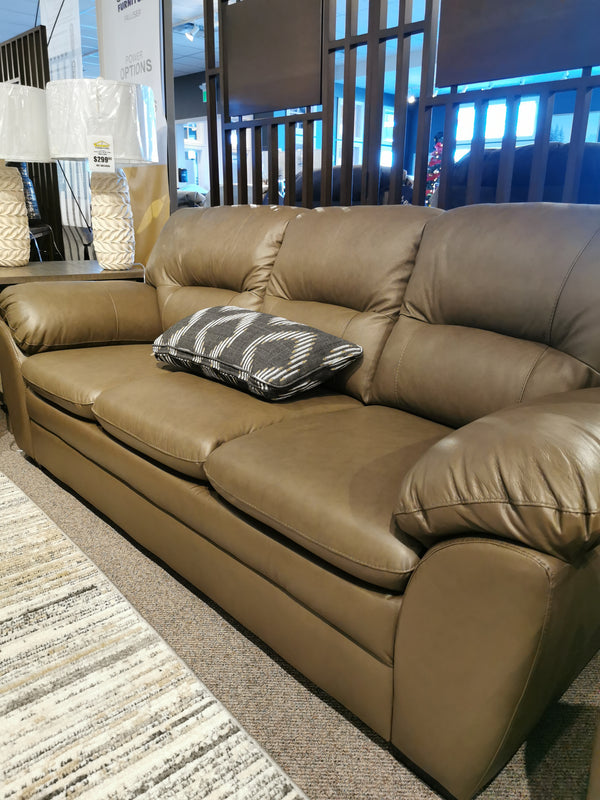 The 77343 Amisk Sofa by Palliser, a brown leather lounger, features a patterned cushion in the showroom.