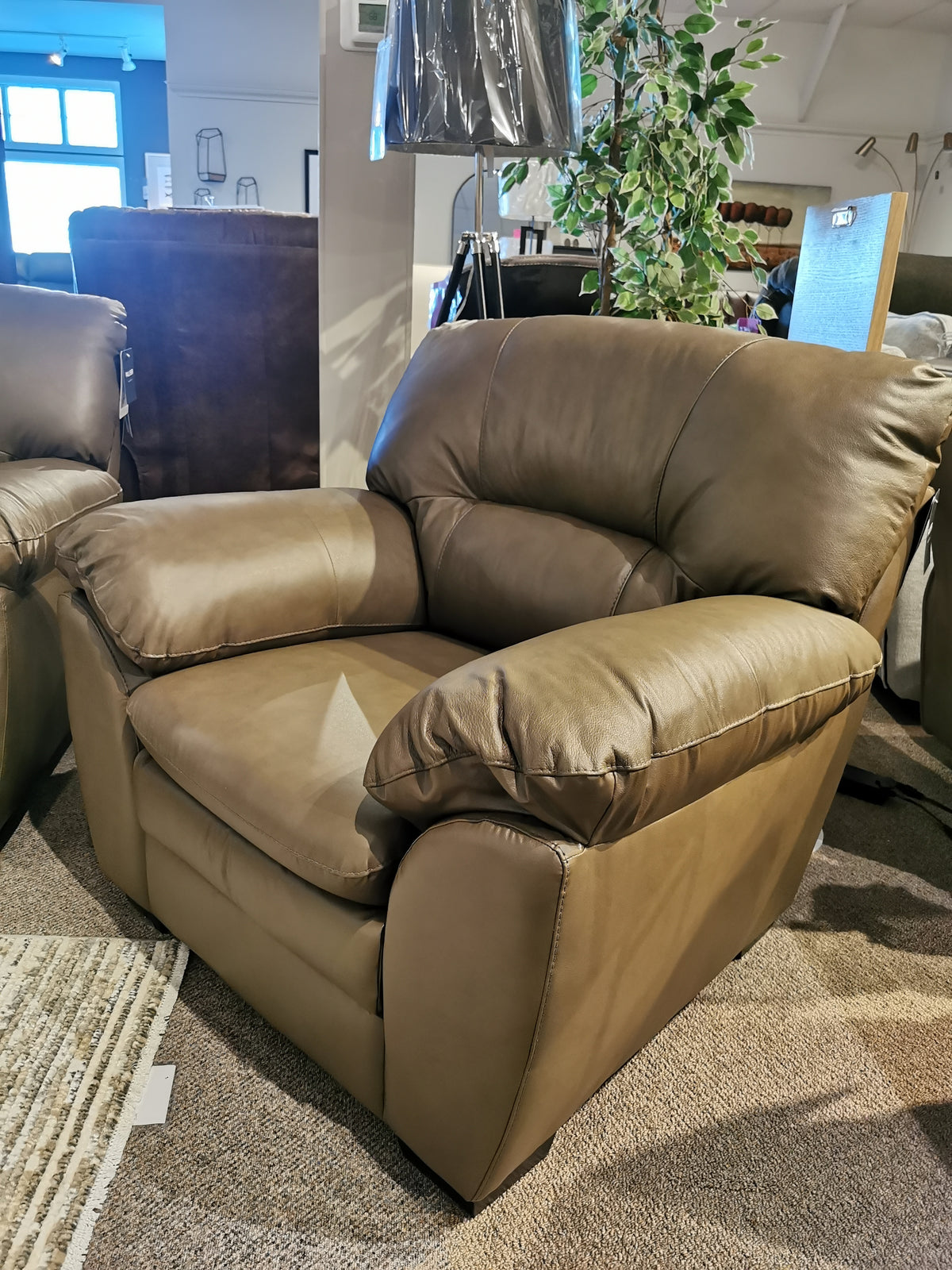 Amisk Chair by Palliser in brown leather, near lounge sofa and plant in a cozy furniture store.