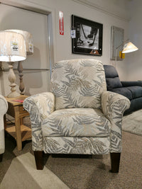 A leaf-patterned armchair is in a showroom, flanked by a floor lamp and the 424 Fletcher Power Hi-Leg Recliner by La-Z-Boy.