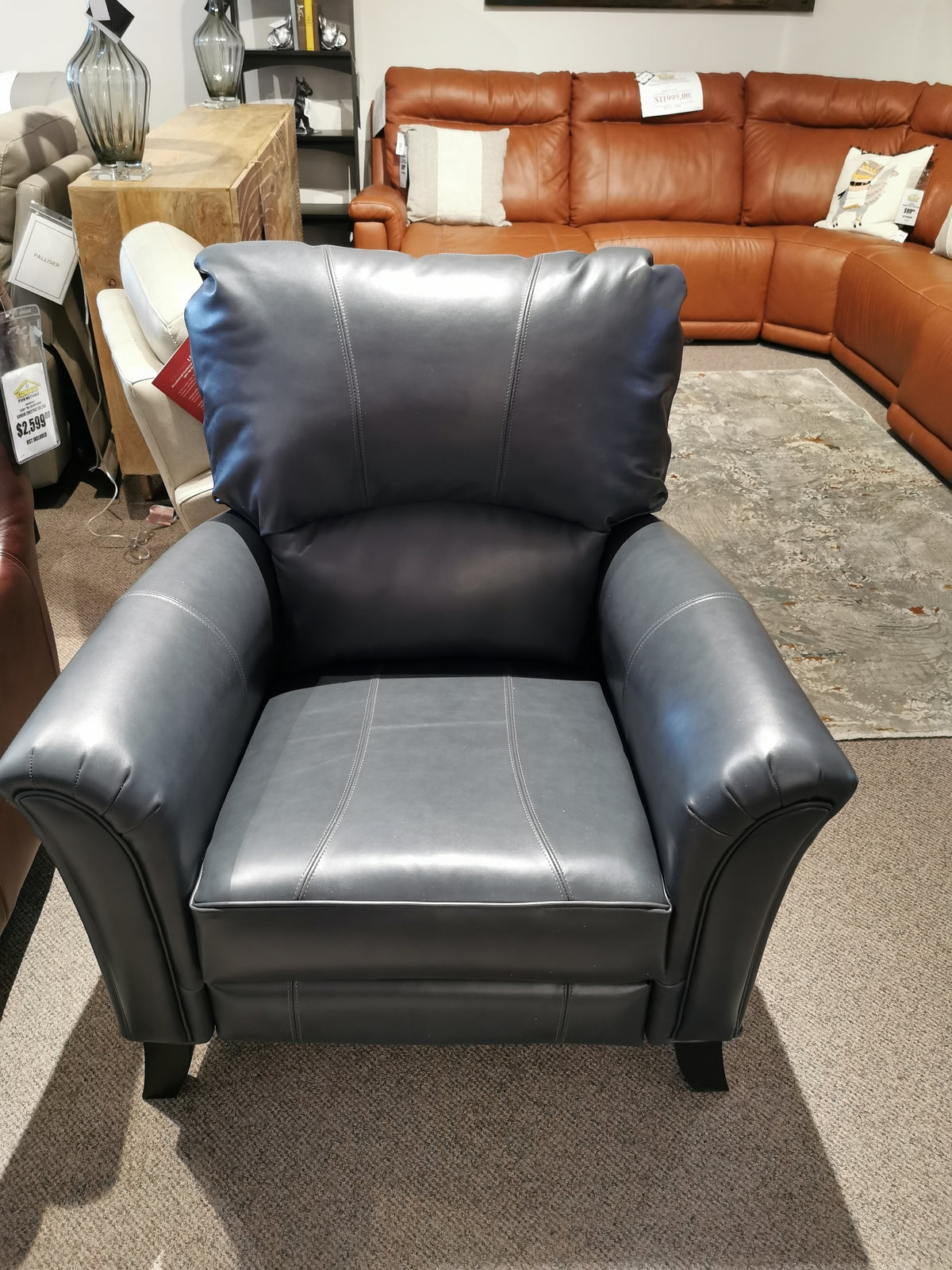 A Decor-rest 3450 Push Back Recliner in black leather features in a showroom, with a sectional sofa in the background.