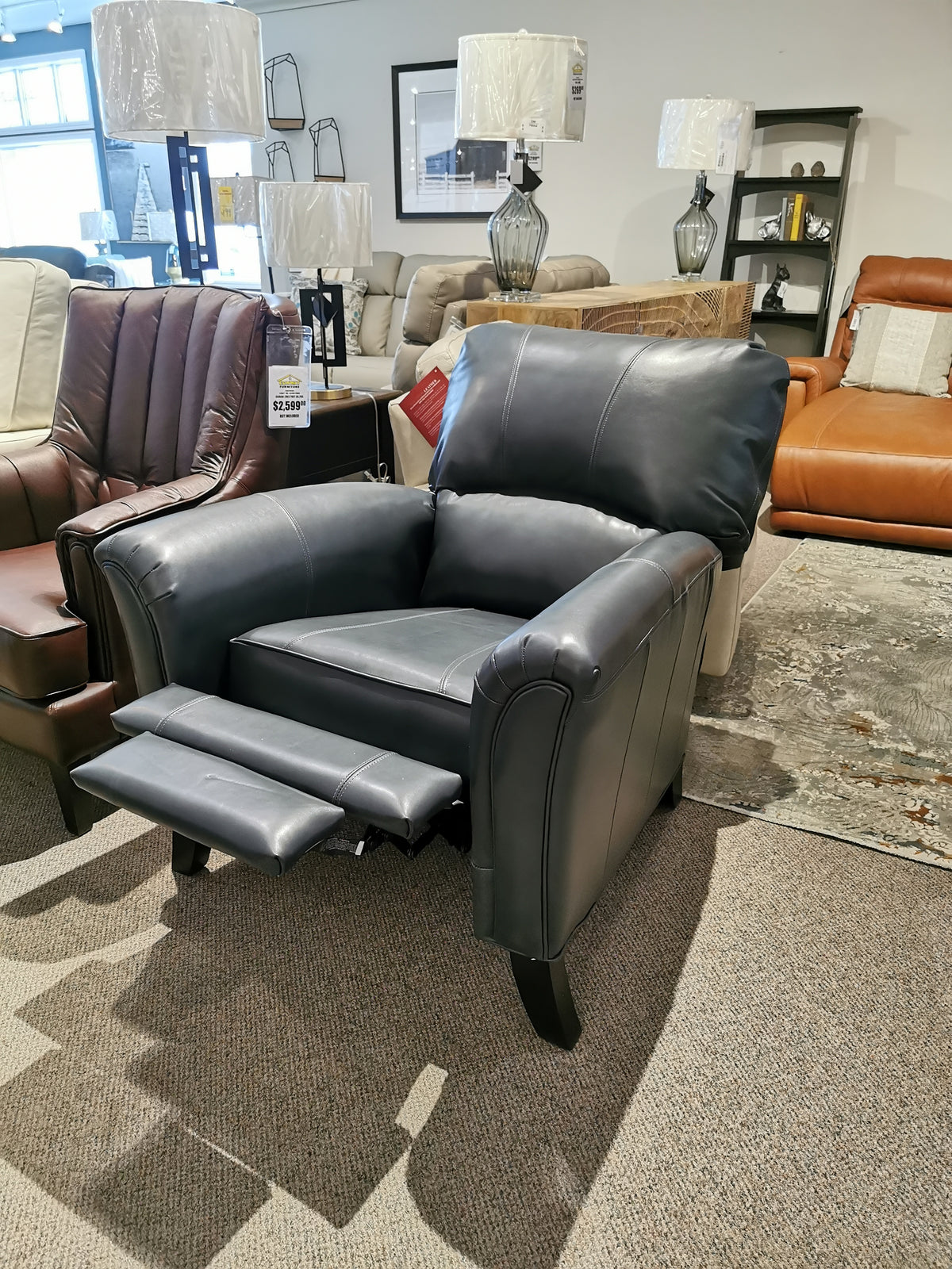 The Decor-rest 3450 Push Back Recliner in black, with a footrest and sinuous springs, graces a stylish showroom.