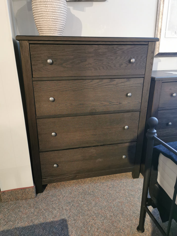 Vaughan Bassett's Fundamentals 4 Drawer Chest in dark wood, featuring deep drawers and metal knobs in a cozy room.