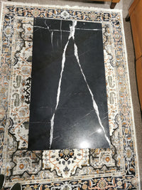 A T5760 Kira Cocktail Table by Magnussen, black marble with white veining, rests on a patterned rug.