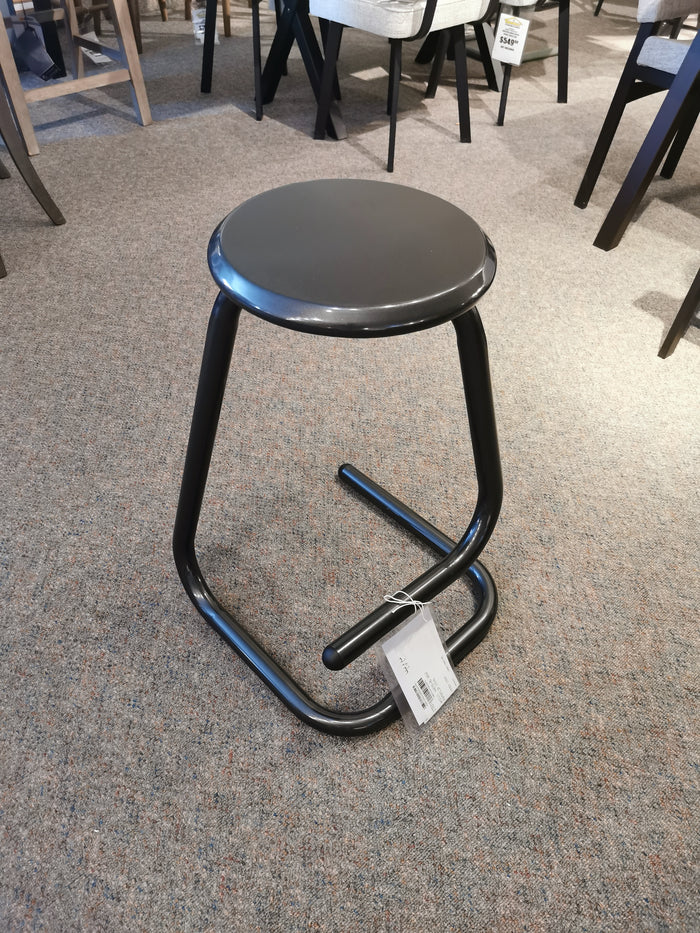 A limited edition Amisco 44070-26 Paperclip Stool with round seat and metallic legs sits on a carpet in a furniture store.