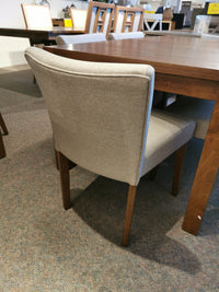 A beige upholstered chair with rubberwood legs sits beside a walnut table, both part of the Bloc Dining Package by Donald Choi.