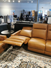 A tan reclining Timberland Power Sofa by Aurora Furniture with a power headrest, surrounded by other seating and a rug.