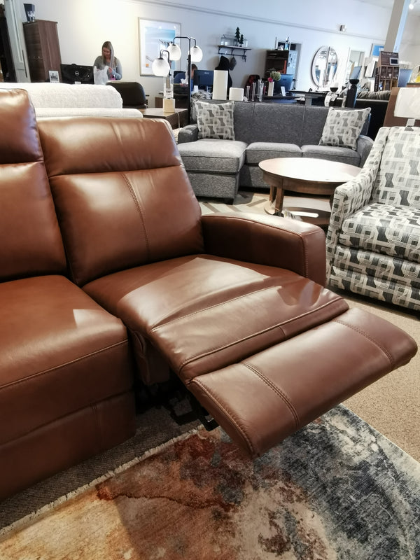 Aurora Furniture's Muskoka Power Loveseat, featuring brown leather and moccasin stitching, in a showroom setting.