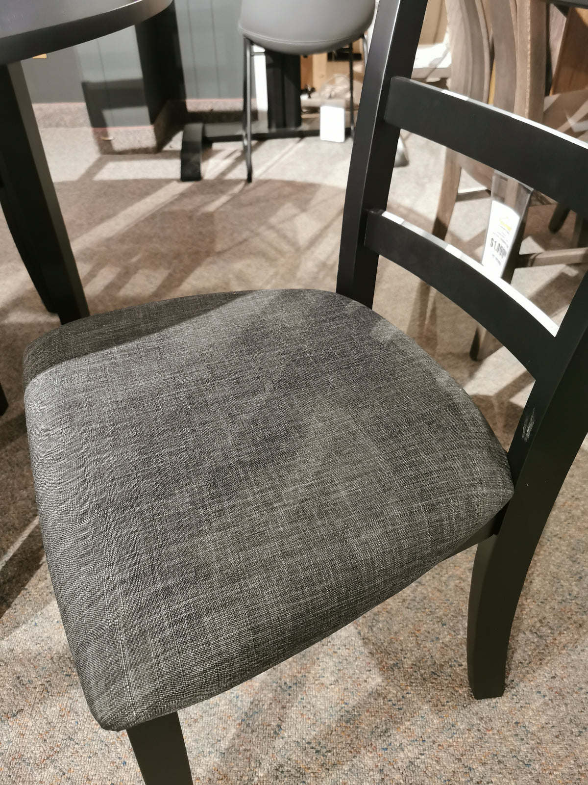 A black wood chair with a gray cushion complements the Donald Choi Emma Dining Package on a carpeted floor.