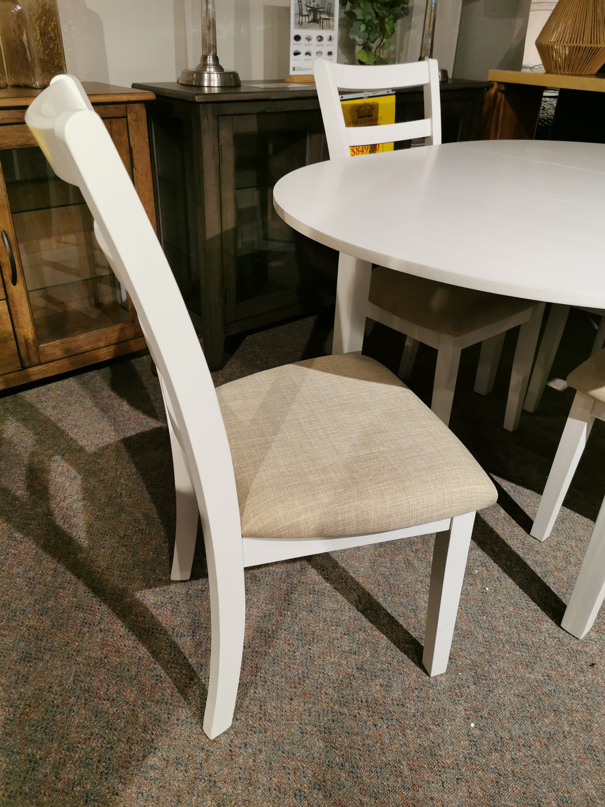 Donald Choi Emma Dining Package white chair with beige cushion beside a round table on carpeted floor.