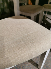 Close-up of a beige upholstered chair seat with fabric texture; Emma Dining Package by Donald Choi appears in the background.