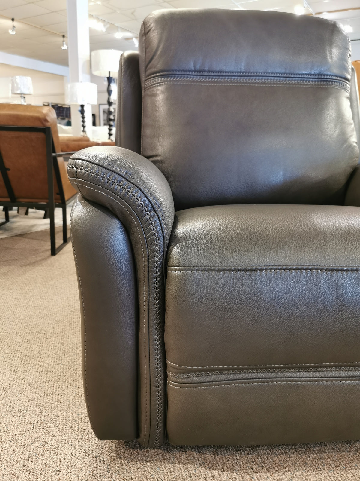 Close-up of Aurora Furniture's Cascade Power Chair, brown leather with visible stitching, on a showroom's carpeted floor.