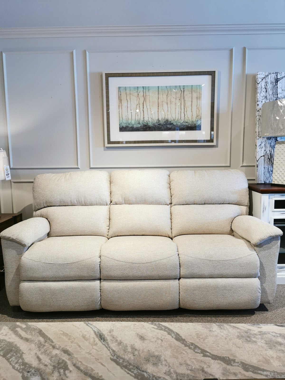 A beige La-Z-Boy 727 Brooks Power Reclining Sofa with custom comfort in a showroom, framed art above, and a lamp-side table nearby.