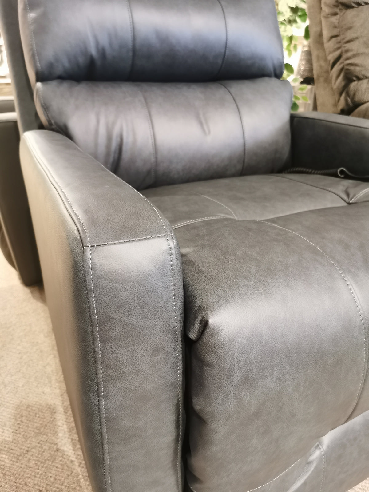 Close-up of Best's Kristisha 9NZ31LV Power Lift Chair in gray leather with cushioned armrests in a showroom setting.