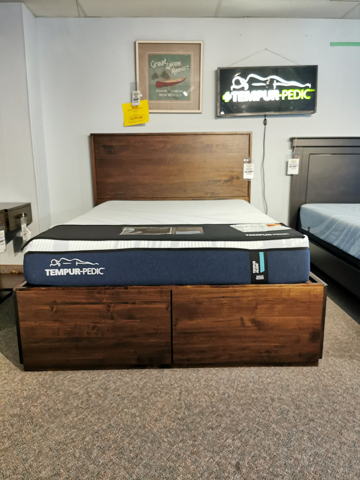 A showroom showcases the Handstone AlaCarte Lisbon Queen Storage Bed with a Tempur-Pedic mattress and neon sign, optimizing storage.