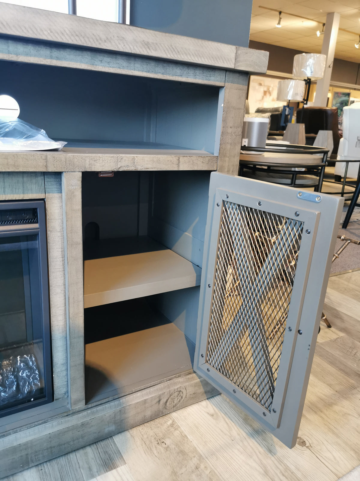 The Telluride Electric Fireplace Mantel by Jofran features an open cabinet with two shelves and a stylish mesh panel.