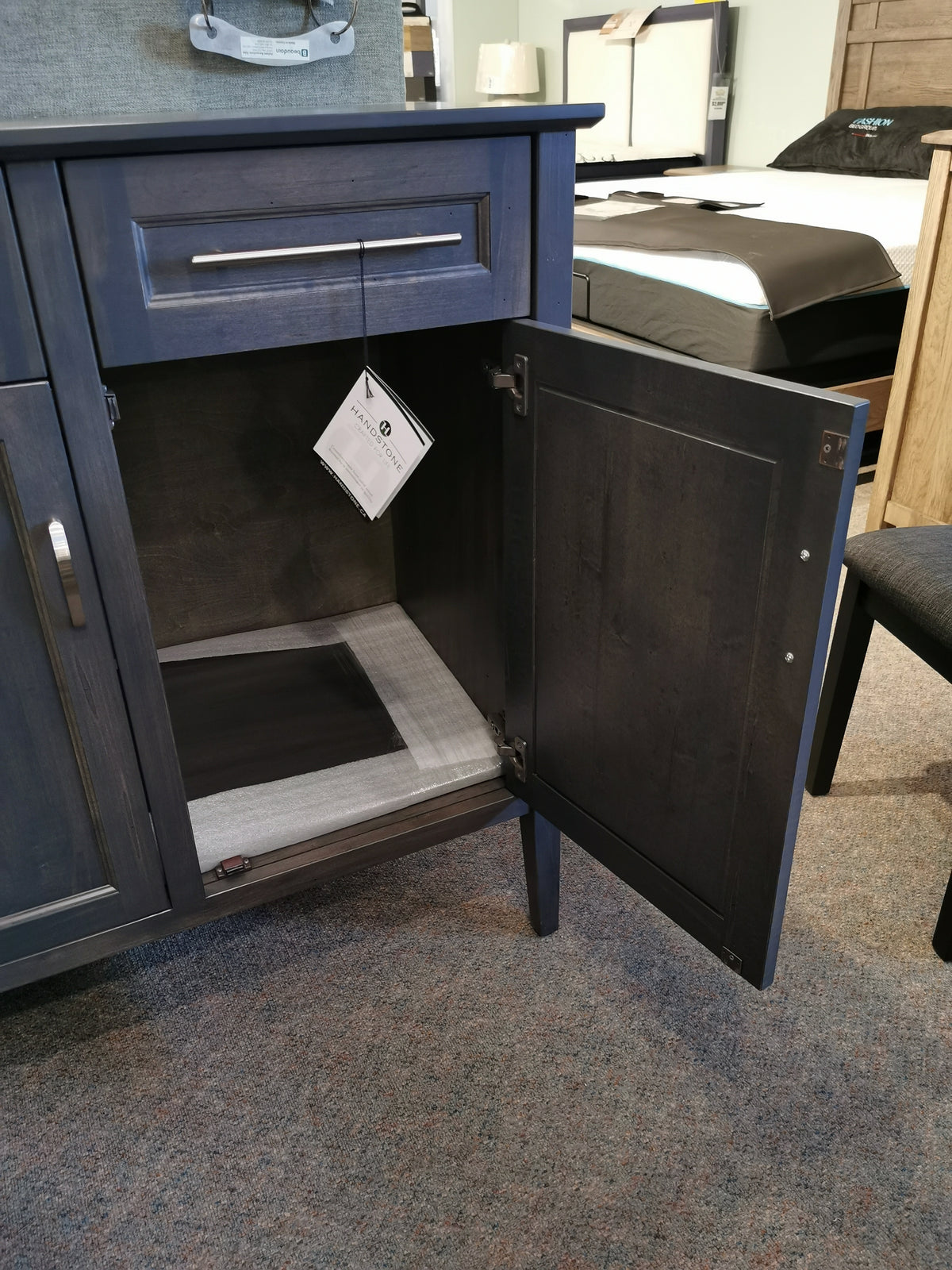 The Handstone Stockholm Soft Close Sideboard in dark blue, featuring an open door and ample storage, has a hanging tag.