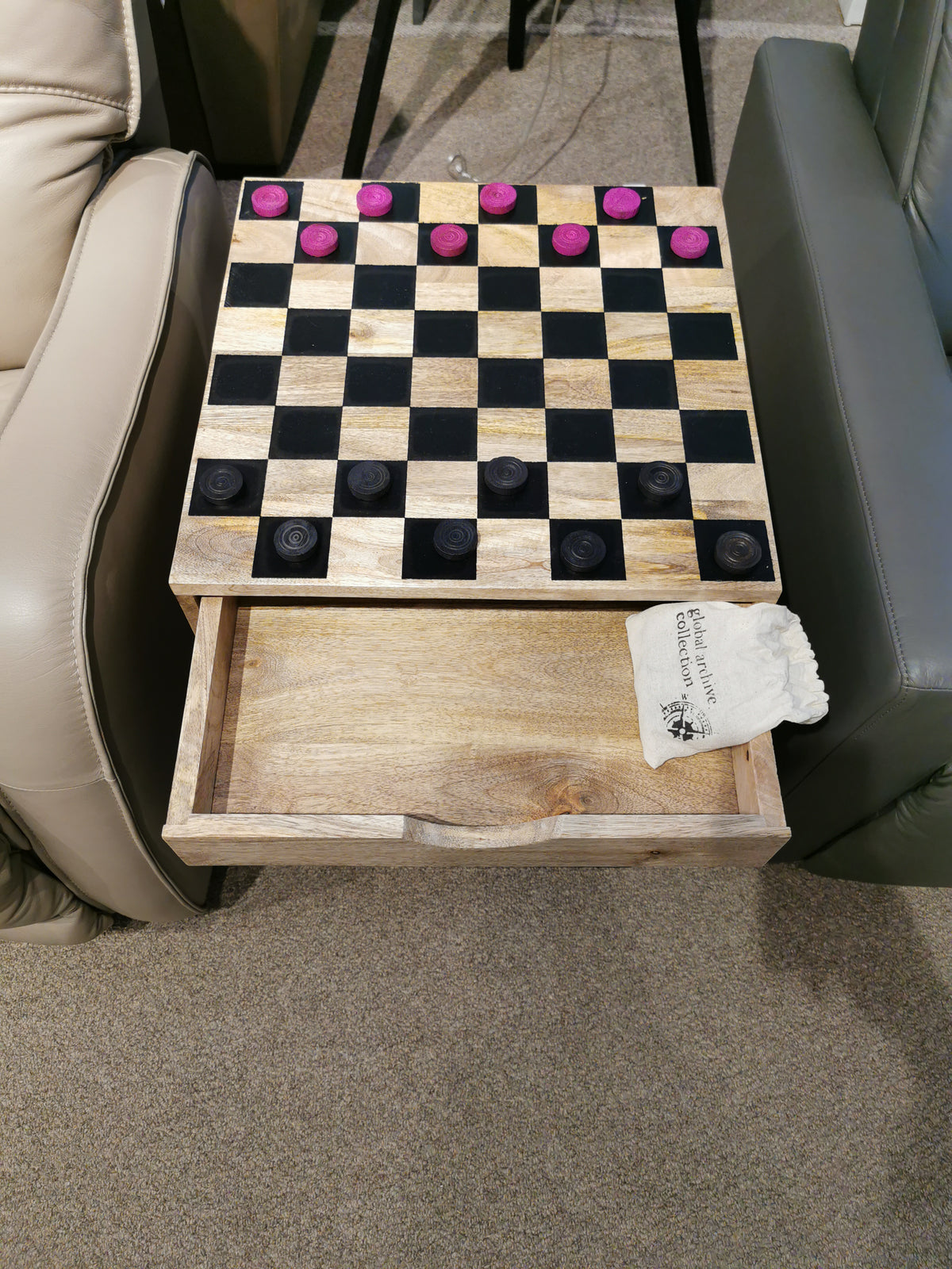 Fairchild Checkerboard C-Table by Jofran, featuring a pull-out drawer with wooden pieces, next to beige upholstery.