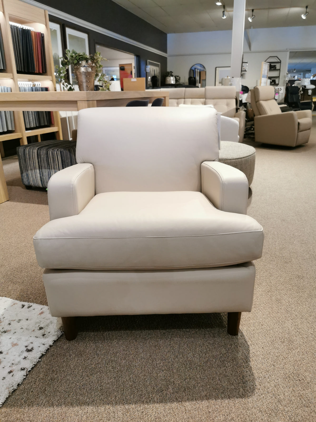 The Abby 77108 Chair by Palliser features a beige T-seat cushion and wooden legs, showcased in a furniture showroom.