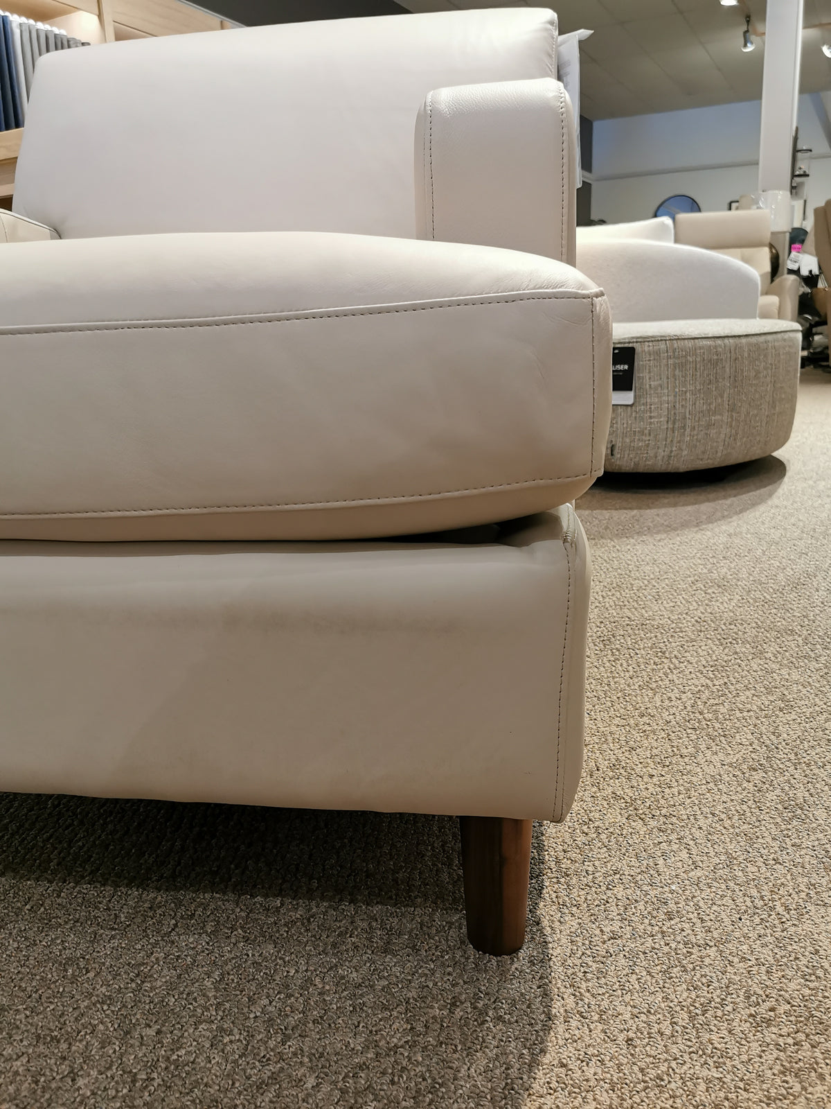 Close-up of Abby 77108 Chair arm by Palliser with T-seat cushion and wood legs on carpet in a store.