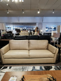 In a showroom, the beige Palliser 77882 Payton Sofa is showcased with other couches and lamps under ceiling lights.