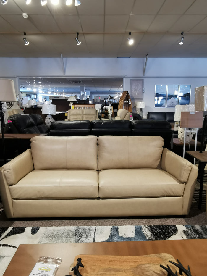 In a showroom, the beige Palliser 77882 Payton Sofa is showcased with other couches and lamps under ceiling lights.